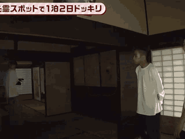 a man in a white shirt stands in an empty room with a sign above him that says " 1 泊 2 日 "