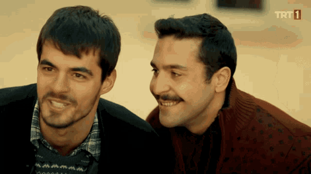two men are smiling in front of a trt logo