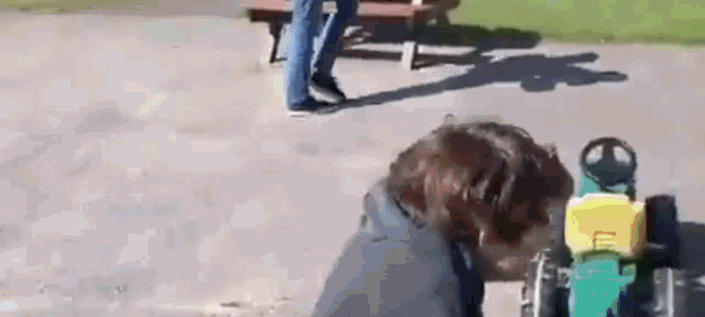 a person is playing with a toy tractor in a park while another person sits on a bench .