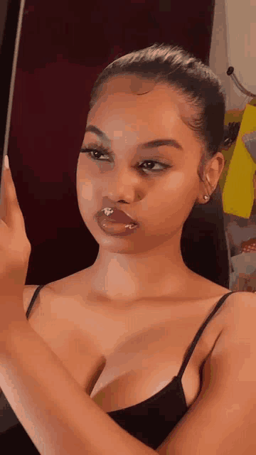 a woman in a black tank top is taking a picture of herself in the mirror .