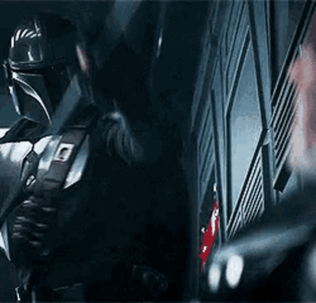 a man in a helmet is standing next to a wall in a dark room holding a gun .