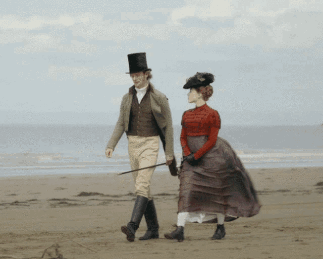 a man in a top hat and a woman in a purple dress walk on the beach