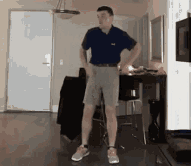 a man in a blue shirt and khaki shorts is standing in a living room