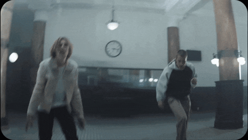 a man and woman are dancing in a dark room with a clock on the wall