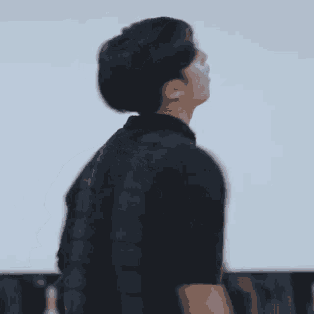 a man in a black shirt is standing in front of a white wall looking up .