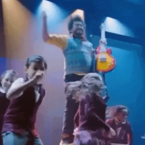 a man is standing on a stage holding a guitar while a group of people are dancing around him .