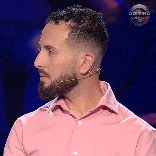a man with a beard is wearing a pink shirt and a microphone on his ear