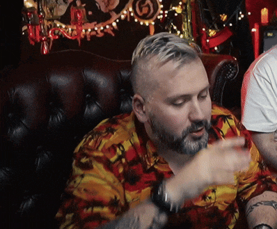 a man with a beard wearing a colorful shirt sits in a chair