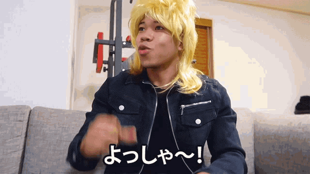 a man wearing a yellow wig and a black jacket is sitting on a couch and says " よっしゃ "
