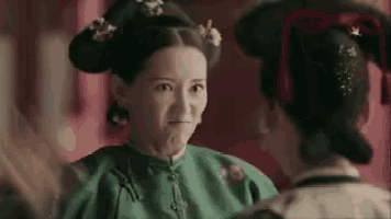 a woman in a green dress is making a face at another woman in a red room .