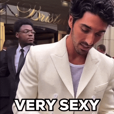 a man in a white suit is standing in front of a sign that says very sexy