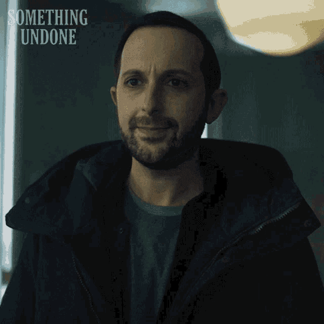 a man with a beard is smiling in front of a sign that says something undone