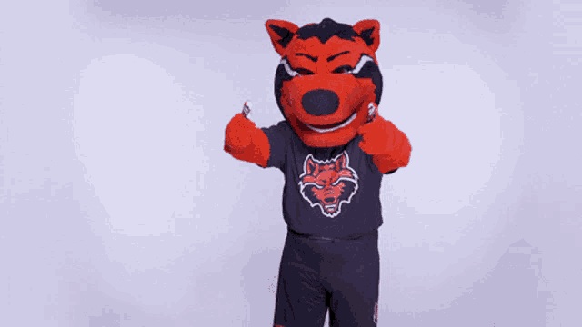 a mascot wearing a black shirt with a wolf head on it gives a thumbs up