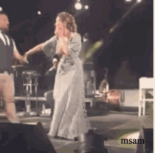 a woman in a striped dress is singing into a microphone while holding hands with a man on stage .