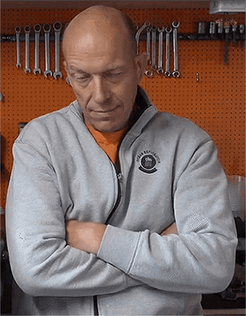 a man with his arms crossed is wearing a grey sweatshirt with a motorcycle emblem on the front