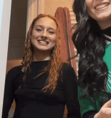 a woman with red hair smiles next to another woman with black hair