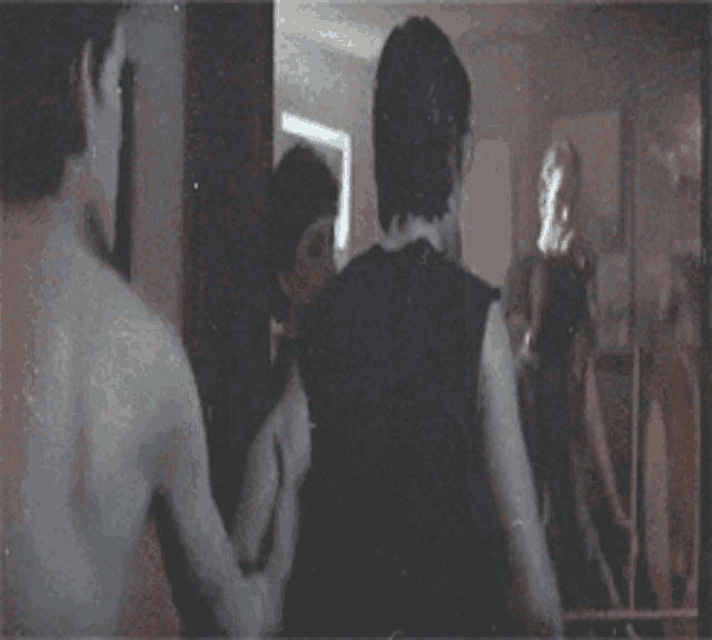 a man in a black tank top stands in front of a mirror