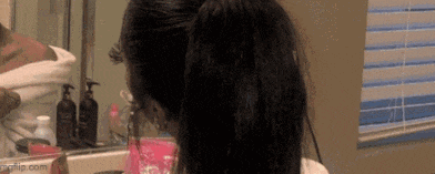 a woman is brushing her hair in front of a mirror .