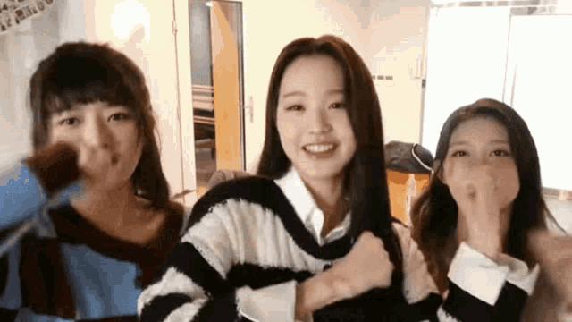 three girls are standing next to each other and one is wearing a striped sweater .