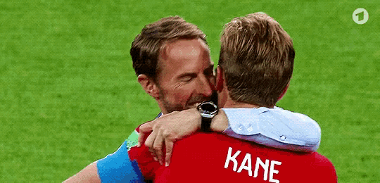 two men are hugging each other on a soccer field . one of the men is wearing a kane shirt .