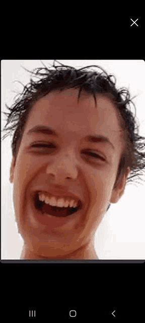 a close up of a young man 's face laughing with wet hair .