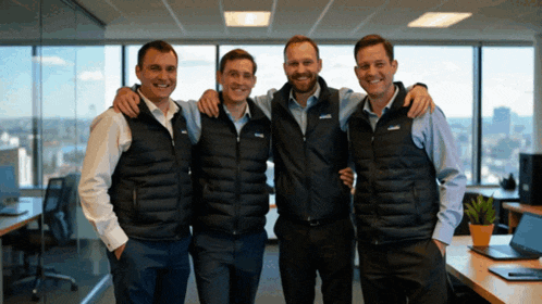 four men are posing for a picture with one wearing a vest that says ' columbia ' on the front