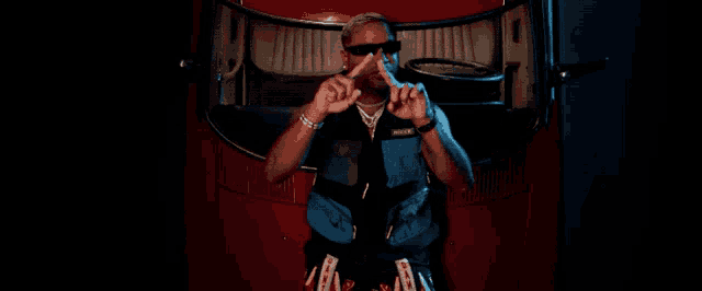 a man wearing sunglasses is sitting in the back of a red car and giving the peace sign