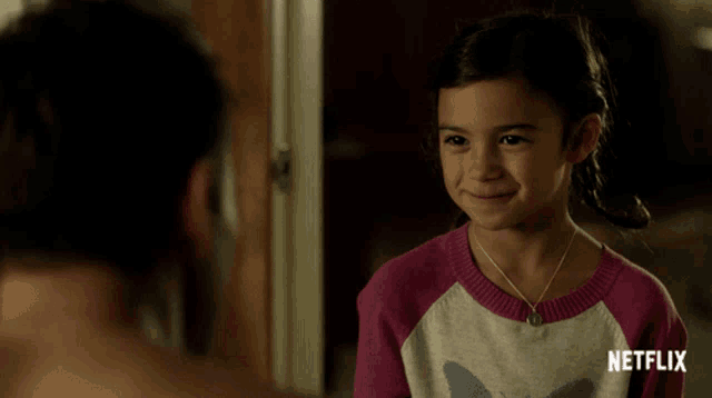 a little girl in a pink and white sweater is smiling in front of a netflix sign
