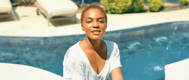a woman in a white shirt is sitting next to a pool and smiling .