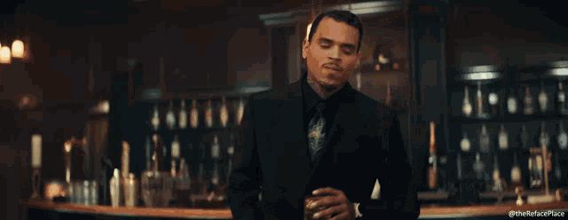 a man in a suit stands in front of a bar with the hashtag #therefuseplace on the bottom