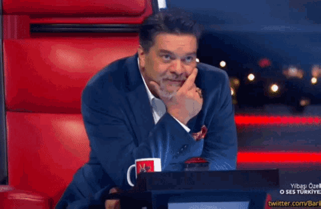 a man in a suit sits in a red chair with a mug that says ntv