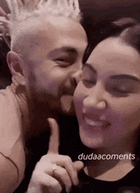 a man is kissing a woman on the cheek while a woman holds her finger to her mouth .