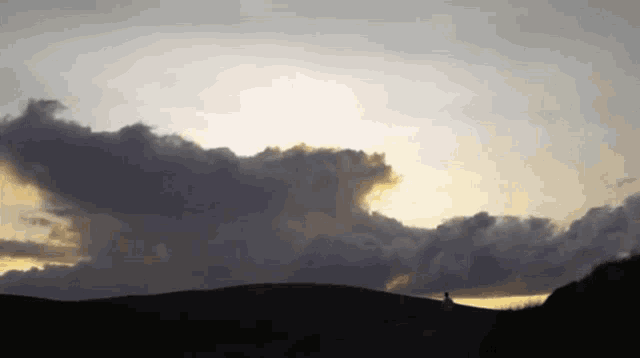 a silhouette of a person standing on a hill with a cloudy sky in the background
