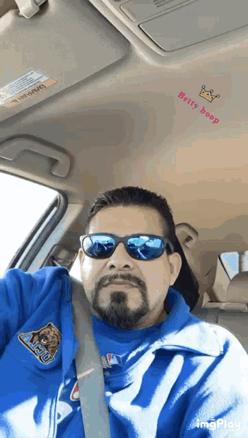 a man wearing sunglasses and a blue shirt with a bear on it is driving a car