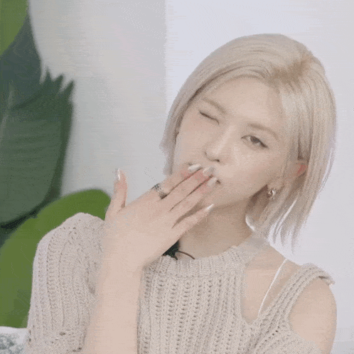 a woman in a sweater blows a kiss with her hand