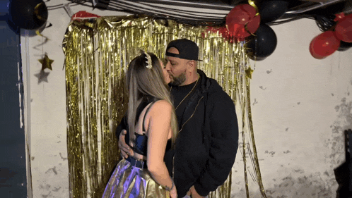 a man and woman are kissing in front of a gold curtain