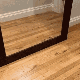 a large mirror on a wooden floor with a black frame