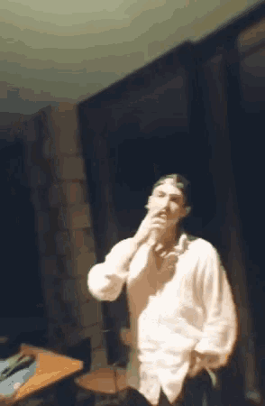 a man in a white shirt is standing in a dark room smoking a cigarette