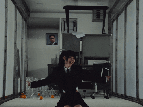 a woman sitting on the floor with her arms outstretched and a picture of a man on the wall behind her
