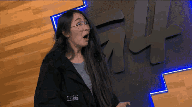 a woman wearing glasses and a black jacket stands in front of a sign that says ff