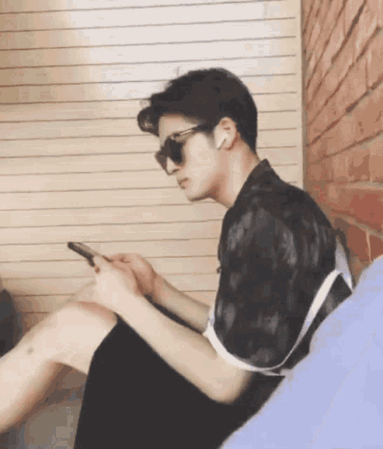 a man wearing sunglasses sits on a couch looking at his cell phone