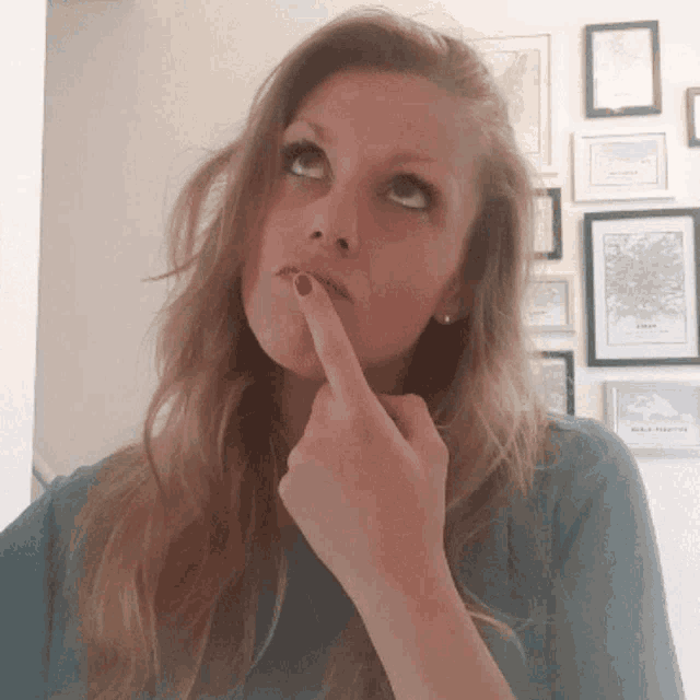 a woman 's finger is on her chin in front of a wall of framed pictures