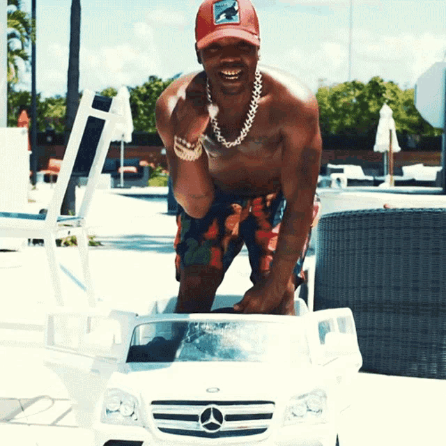 a shirtless man in a red hat is standing next to a toy mercedes