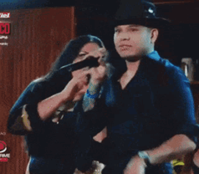 a man in a cowboy hat is singing into a microphone while a woman watches