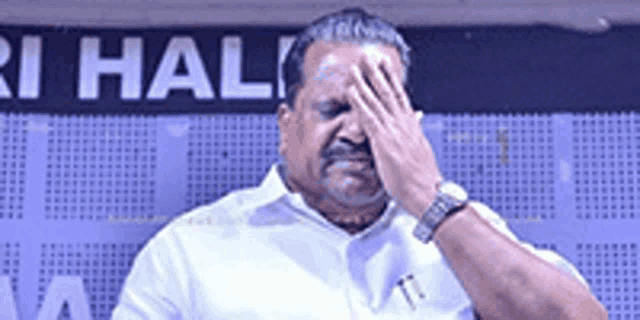 a man in a white shirt covering his face with his hand