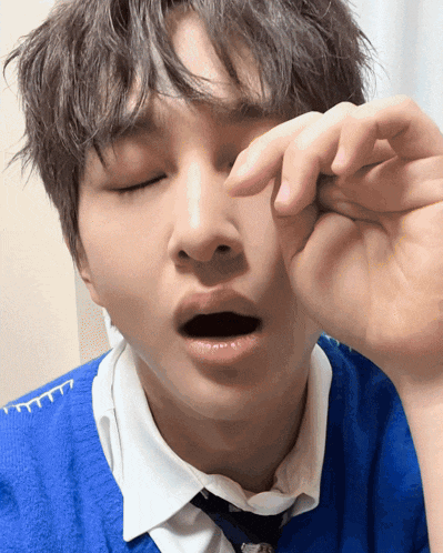 a young man wearing a blue sweater and tie is rubbing his eye
