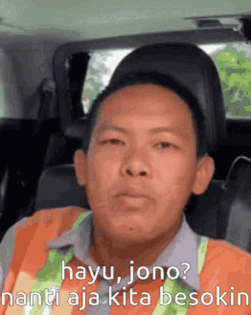 a man in an orange vest is sitting in a car with the words hayu jono written below him