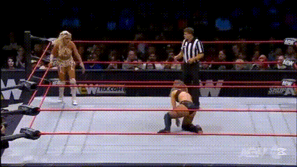a wrestler is kneeling down in a wrestling ring while a referee watches .