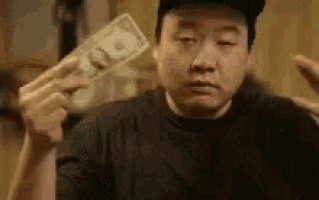 a man is holding a dollar bill in his hand and making a funny face .