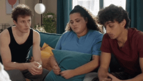 three people are sitting on a blue couch and one of them has a tattoo on her arm